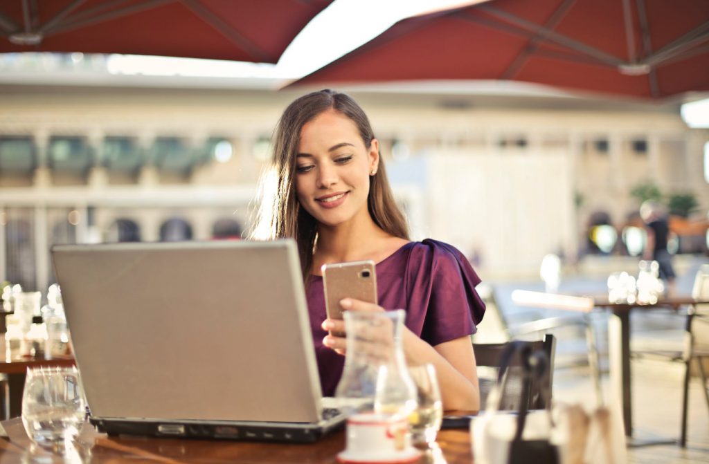 uśmiechnięta kobieta z telefonem i laptopem w kawiarni